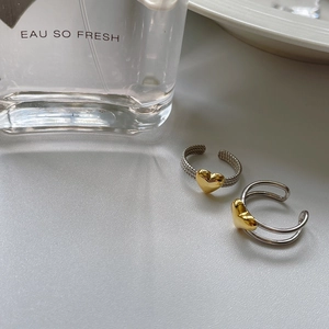 Detail of silver twisted open rings with golden hearts next to a perfume bottle