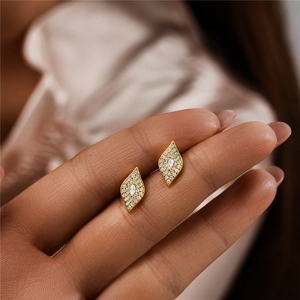 Close-up of gold leaf-shaped stud earrings with marquise-cut cubic zirconia in fingers