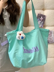 Detail of mint green tote bag featuring purple script and plush animal charm