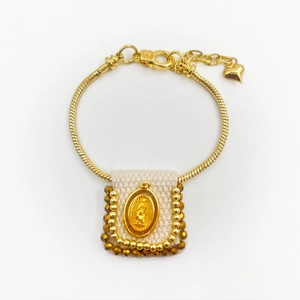 Detail of gold snake chain bracelet with Virgin Mary fabric charm and heart pendant