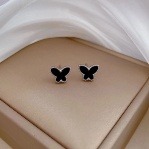 Macro shot of butterfly stud earrings with black inlay and silver beaded edges on silk
