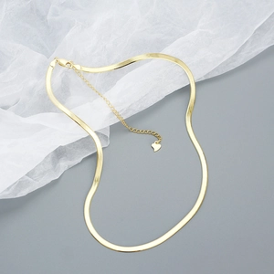 Close-up of golden flat snake bone chain necklace with heart charm and extender on soft fabric