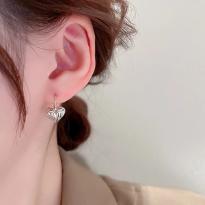 Close-up of minimalist silver heart earring with crumpled texture on female model ear