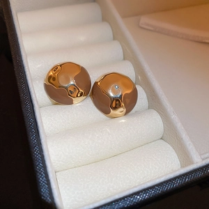 Vue macro de boucles d'oreilles géométriques en émail doré et marron dans un coffret blanc