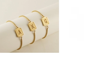 Detailed macro of gold-plated rectangular initial charms with frosted sand finish texture