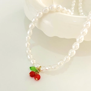Elegant pearl necklace featuring red cherry pendant draped on a white porcelain bowl