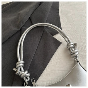 Detailed view of silver bow-knot handle and metallic zipper on a shiny PU leather handbag
