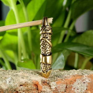 Detail of golden snake wrapped dagger pendant with scale texture on a rustic brick