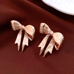Close-up of rose gold bow earrings with a textured metallic finish on a ceramic plate