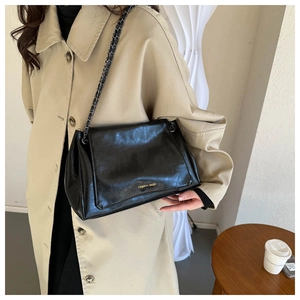 Black oil wax leather shoulder bag with gold chain strap shown on a female model