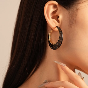 Close-up of model wearing large C-shaped resin earrings with gold-tone metal and tortoiseshell pattern