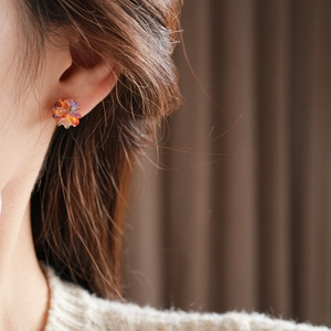 Close-up of a model wearing colorful floral stud earrings with crystal petal accents