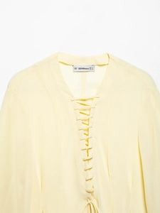 Detailed close-up of lace-up design and neck label on a light yellow summer shirt