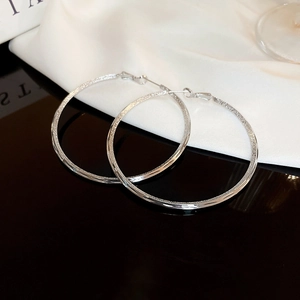 Detailed macro view of large silver hoop earrings featuring polished and frosted textures