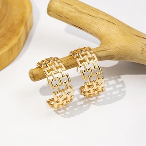 Macro detail of gold C-shaped earrings with hollow chain design on a branch