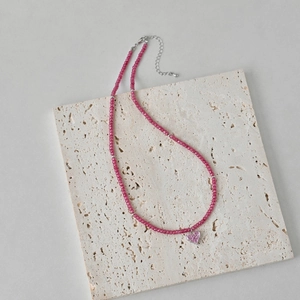 Detail of pink crystal beaded necklace with silver heart pendant on stone tile