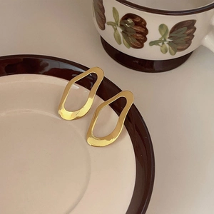 Close-up of golden irregular hollow earrings with hammered texture on a ceramic plate