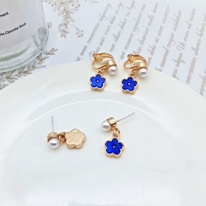 Close-up of elegant blue floral earrings with pearls on a white ceramic plate