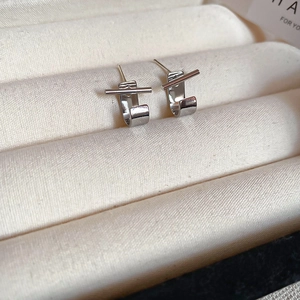 Macro shot of silver geometric earrings with minimalist bar and circle cross design