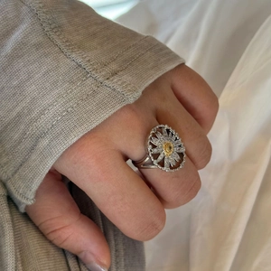 Close-up of elegant silver daisy ring with gold center and crystals on woman's finger
