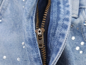 Gros plan sur la fermeture éclair YKK en métal et les strass sur une veste en jean bleu