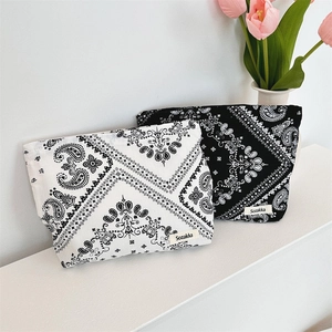 Dettaglio di trousse in tela con motivo paisley, chiusura a zip ed etichetta del marchio