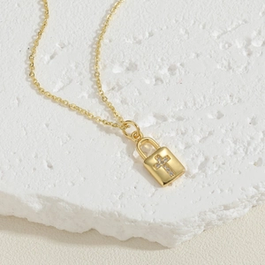 Macro detail of 14K gold plated square lock pendant with zircon cross on stone surface