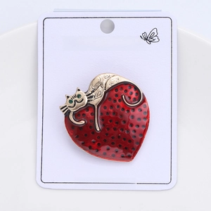 Detail of a gold cat brooch with red enamel and black dots on a display card