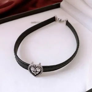 Vintage black leather choker featuring a silver cross heart pendant on silk background