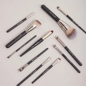 Flat lay of professional makeup brushes with black handles and silver ferrules on grey background