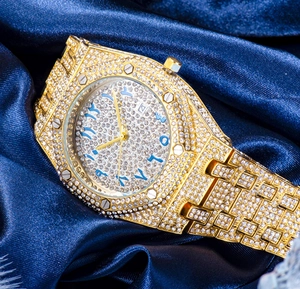 Macro shot of gold iced-out watch with blue Arabic numerals and date window on blue satin