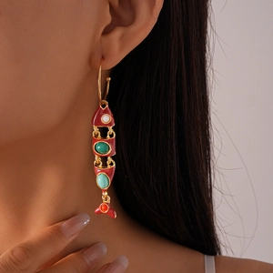Detail of red enamel fish tassel earring in gold metal finish on a model's ear
