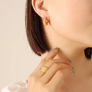 Gold-plated C-shaped earrings with zircon and a wide striped ring on a model
