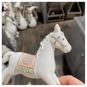 Detail of white resin rocking horse ornament with knit texture and pink sequin saddle