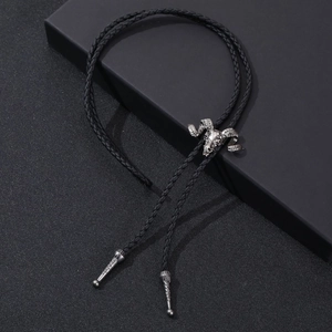 Close-up of vintage silver ram skull bolo tie with black braided cord on dark surface