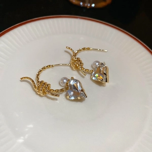 Detail view of golden twisted earrings featuring a large heart-shaped crystal and pearl