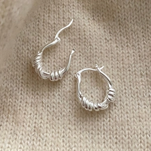 Macro shot of silver twisted rope hoop earrings resting on a beige knit fabric background