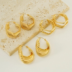 Three pairs of vintage gold-plated stainless steel earrings on a beige stone slab