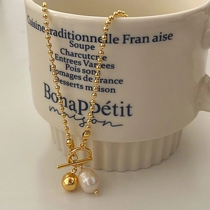 Collier de perles dorées vintage avec pendentif perle et fermoir à bascule sur une tasse