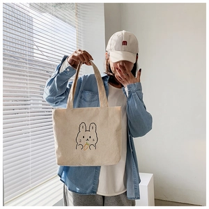 Detail of cute rabbit embroidery on beige corduroy tote bag with minimalist design