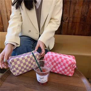 Knitted checkerboard makeup bag with metal zipper closure held by a model in a cafe
