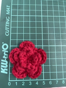 Macro view of 7cm handmade red crochet flower measured on a green grid cutting mat