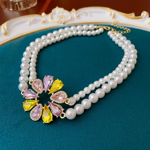 Detail einer zweireihigen weißen Perlenkette mit lila-gelbem Blumenanhänger aus Metall