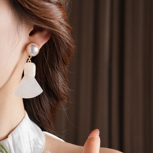 Close-up of pearl drop earrings with fan-shaped resin pendant and elegant gold frame
