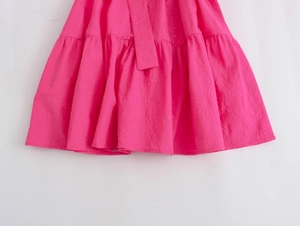 Detailed macro shot of pink textured mini dress featuring elegant ruffle hem and embossed floral pattern
