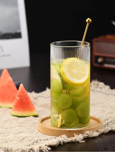 Vaso de cristal con rayas verticales, bebida de limón y agitador dorado en posavasos