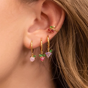 Close-up of gold fruit-themed earrings set with colorful strawberry and cherry studs