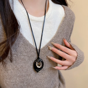 Close-up of a minimalist black teardrop pendant with silver ring on a leather cord