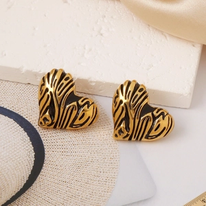 Detailed view of heart-shaped gold earrings with black zebra pattern on stone background