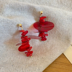 Detail of red beaded fringe earrings with golden studs on a rustic linen background